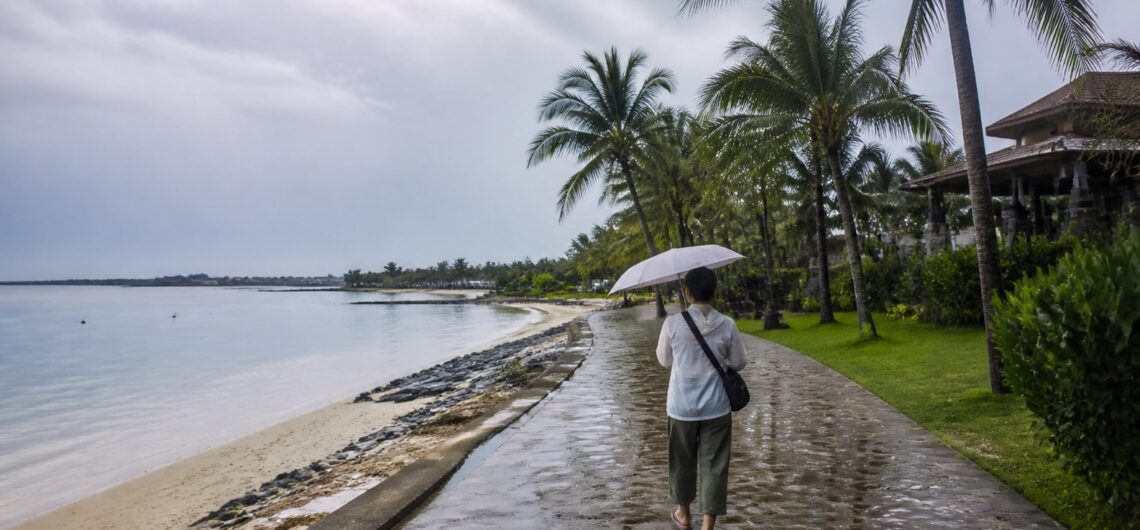 雨季のセブ島の海辺を傘をさして歩く旅行者