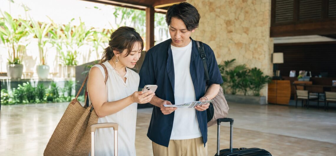 セブ島のホテルロビーでスマートフォンと旅程表を確認する30代の日本人旅行者カップル