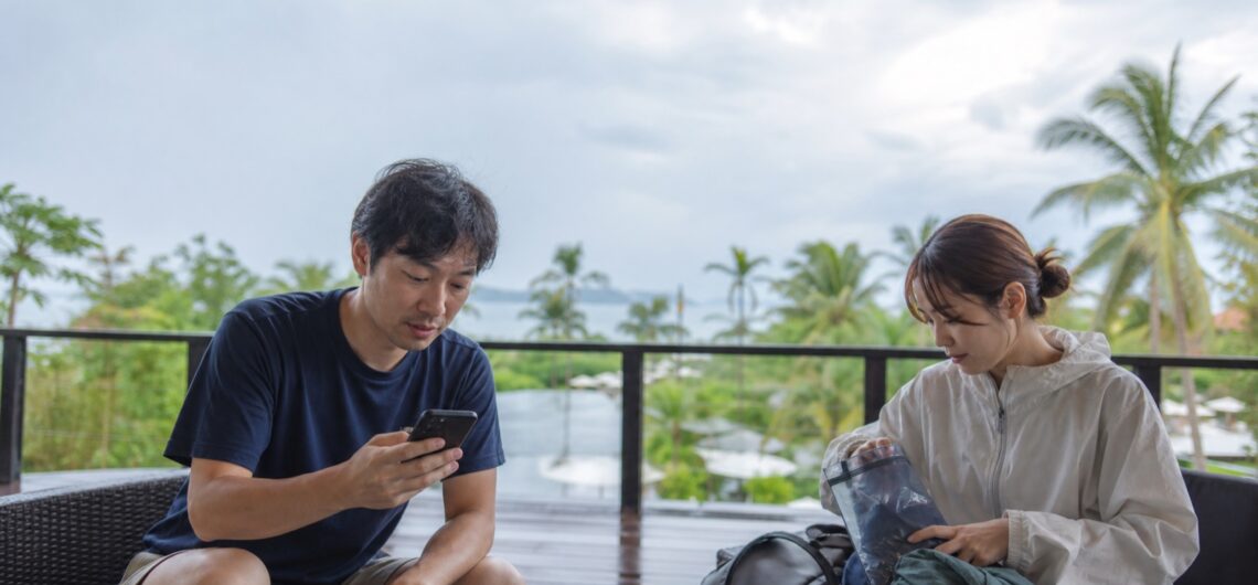 7月のセブ島旅行で天気予報と雨具を確認する30代の日本人カップル(生成画像)