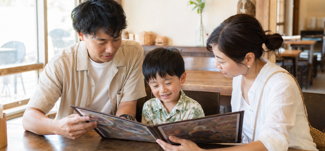 木のテーブルでメニューを見る親子三人